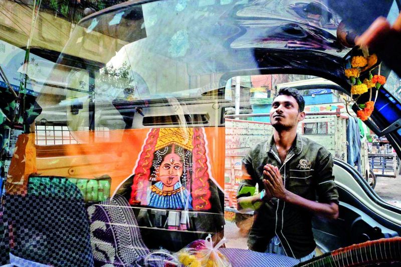 A man prays to the Goddess on the streets of Lucknow, with the reflection of it falling on the glass of a car parked in front.
