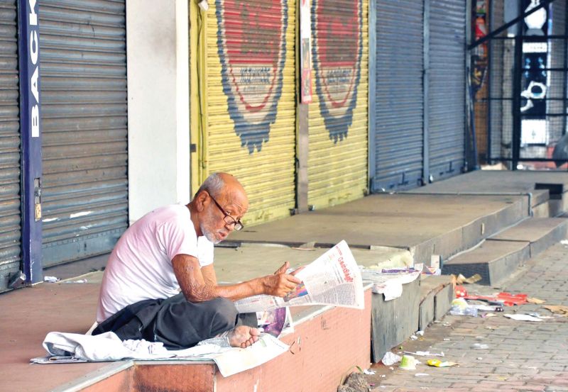 An old man flips through the newspaper as shops remain shut at an otherwise busy Mananchira in Kozhikode on Monday.