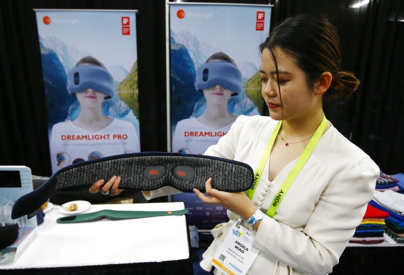 Angela Miao, of Dreamlight, demonstrates their new sleep mask Dreamlight Pro that uses light, sound and genetics so you fall asleep faster and wake up with more energy according to the company, at the CES Unveiled at CES International Sunday, Jan. 6, 2019, in Las Vegas. (AP Photo/Ross D. Franklin)