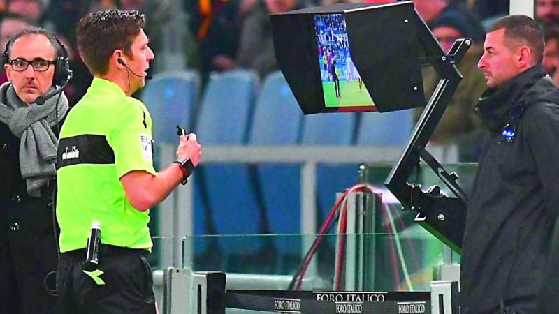 The on-field referee checks a replay on the monitor near the touchline.