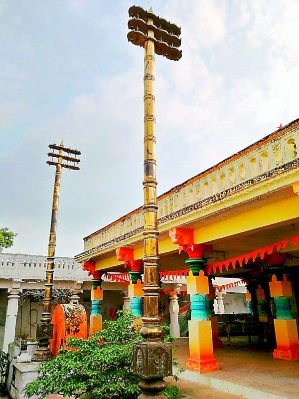. The two Dwaja sthambas stand tall against the colourful old pillars.