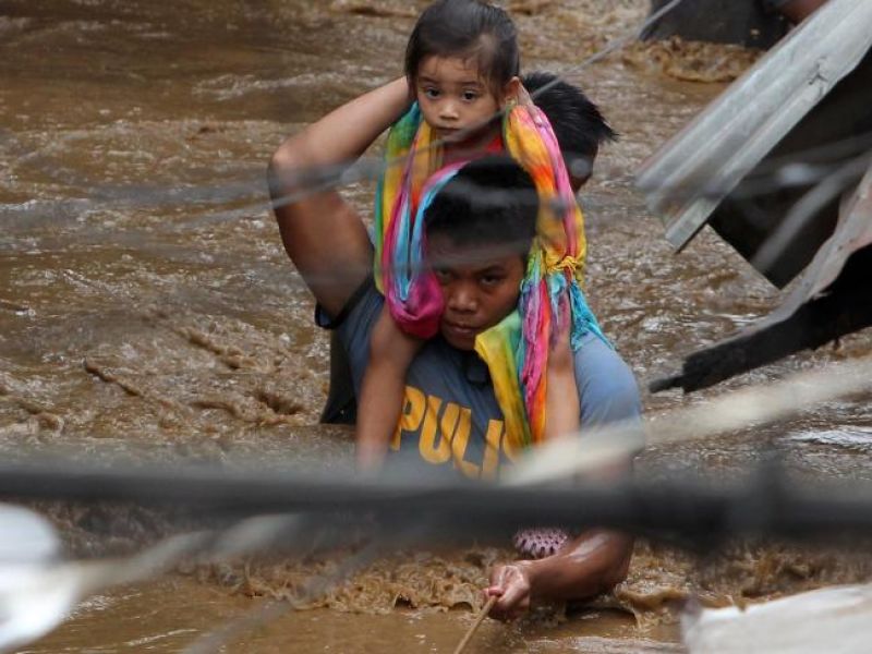 A policeman carries a young girl as he wades through a flooded street in Cagayan City after the Cagayan River swelled caused by heavy rains brought by Tropical Storm Tembin. (Photo: AFP)