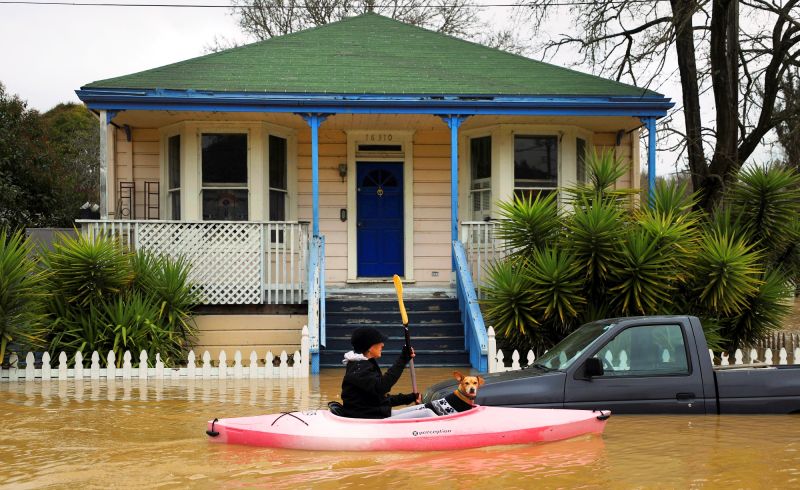 A woman with a dog sails a kayak on a flooded street in Guerneville, north of San Francisco. (Photo: AP)