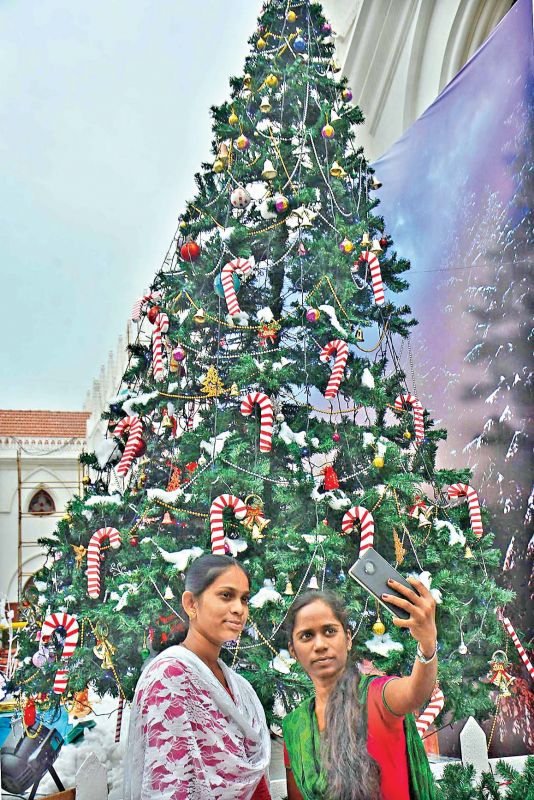 Two woman take selfies with a Christmas tree in the background.