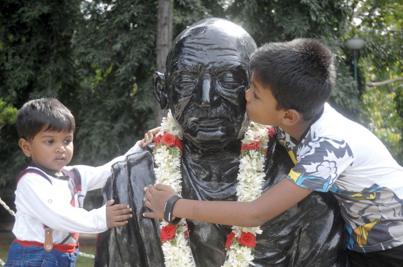 (Top) Boys hug the Gandhi statue on MG Road in Bengaluru on Tuesday. (Right) City Mayor Gangambike Mallikarjun garlands Gandhi statue on MG Road in Bengaluru on Tuesday  (Image DC)