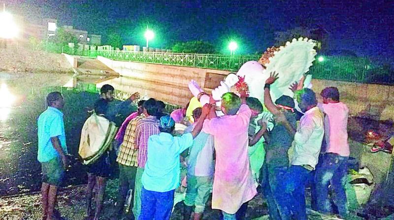 Devotees immerse a huge idol of Lord Ganesh manually due to lack of cranes at Neknampur lake on Tuesday. There was no proper lighting and the lake was strewn with garbage. at Neknampur lake on Tuesday. There was no proper lighting and the lake was strewn with garbage.