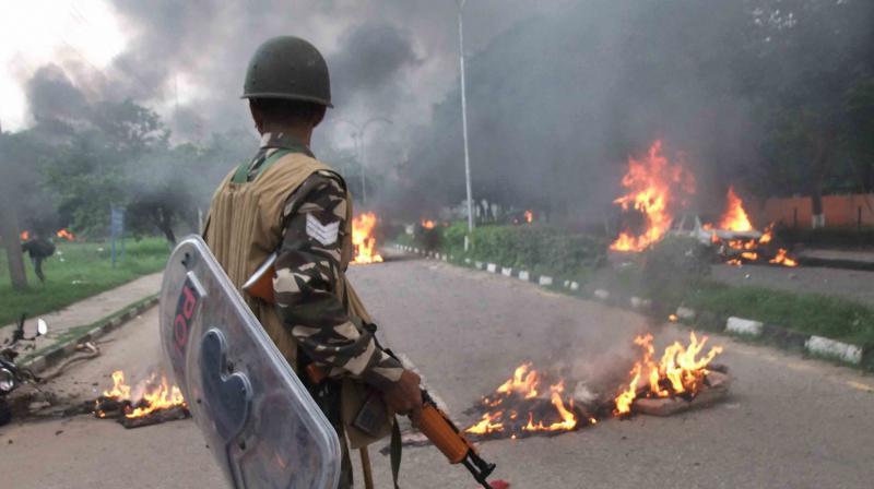 A Security personnel stands towards vehicles burning in violence following Dera Sacha Sauda chief Gurmeet Ram Rahims conviction in Panchkula on Friday. (Photo: PTI)