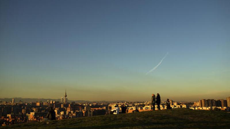 A layer of smog covers the skyline as people stand atop a hill at the Tio Pio park at sunset in Madrid. (Photo: AP)