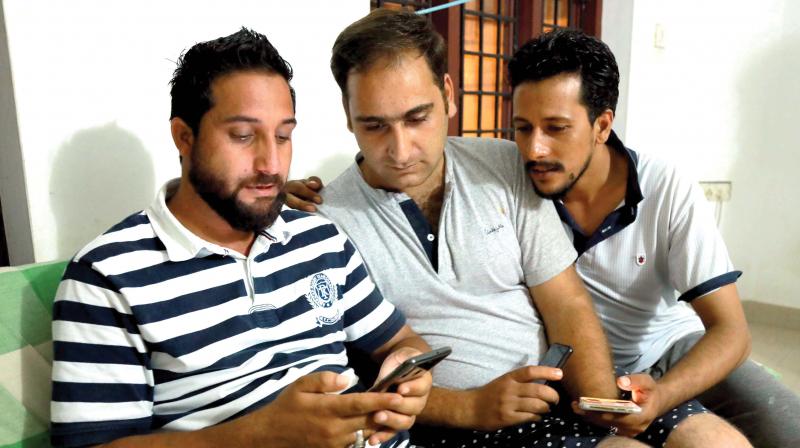 Wani Nisar, Ishfaq Ahammed Malik and Inayat Farooq from Kashmir watch news on the situation of Kashmir on their mobile phones in Mattancherry on Monday.(Photo:  ARUN CHANDRABOSE)