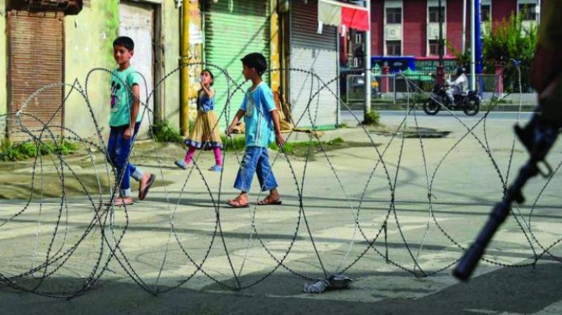 Children walk past concertina wire during restrictions following the abrogation of the provisions of Article 370 in Srinagar on Friday. (Photo: PTI)