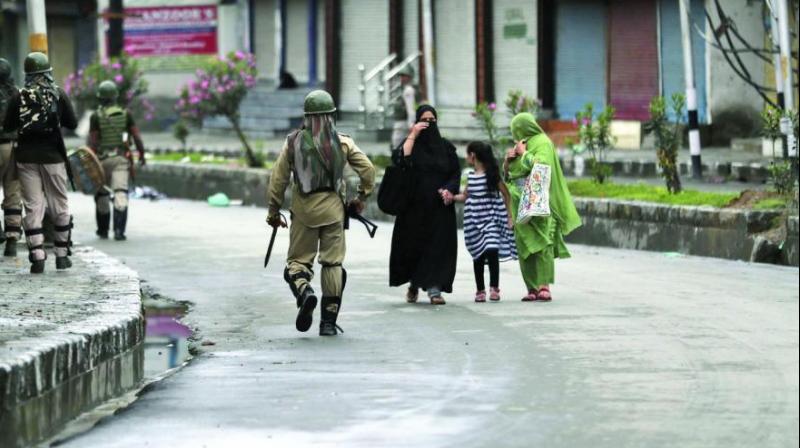 Kashmiris walks past paramilitary troops patrolling a street in Srinagar on Saturday. (Photo: AP)
