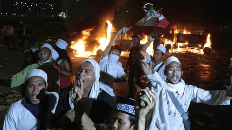Muslim protesters chant slogans near burning police trucks during a clash with the police outside the presidential palace in Jakarta. (Photo: AP)