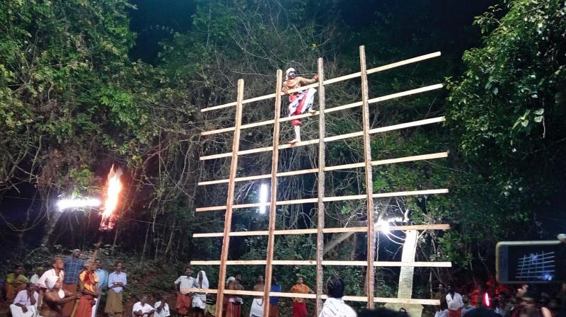 The Bhagavathi Thira climbs upon the wooden crossbar as part of the ritual dance Azhimuri Thira.