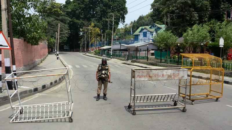 A security person stands guard at a blocked road Outside United Nations Office (UNO) during a curfew imposed to foil the Hurriyats protest march against civilians killings, in Srinagar on Friday. (Photo: PTI)