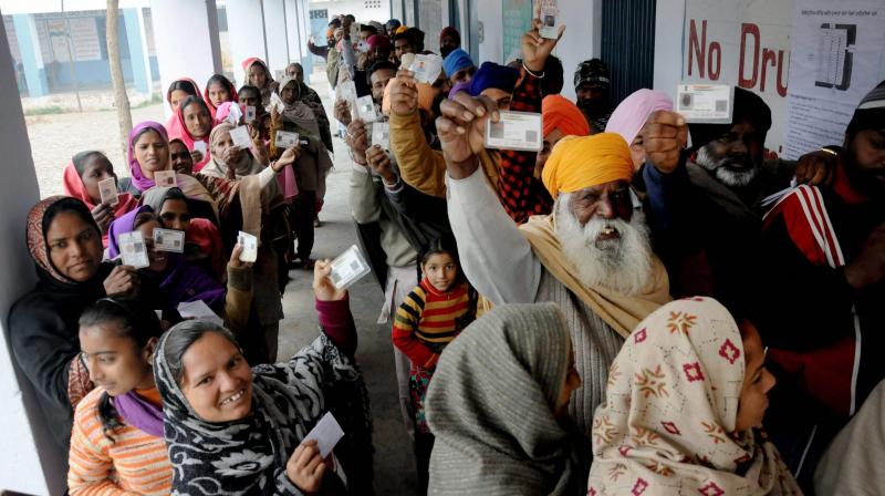 People showing their voter ID cards as they stand in a queue to cast their votes at a polling station in a village, about 25 km from Amritsar, on Saturday. (Photo: PTI)