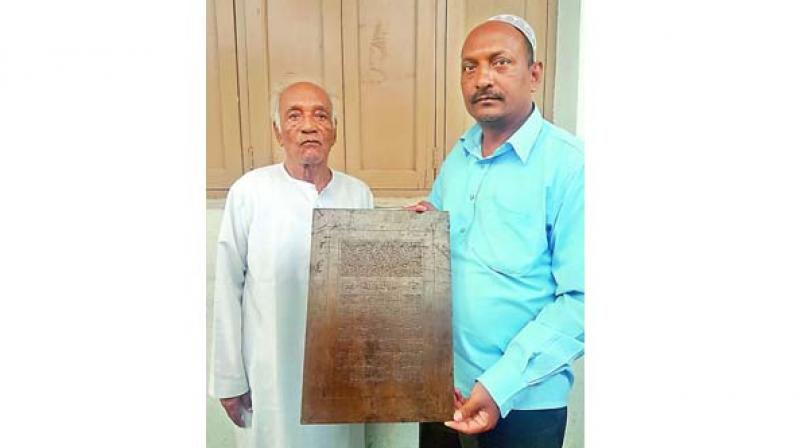 Shabbir Ahmed stands as his son Mohammed Abdul Kareem holds up an iron plaque, where the verses of the Holy Quran were engraved.