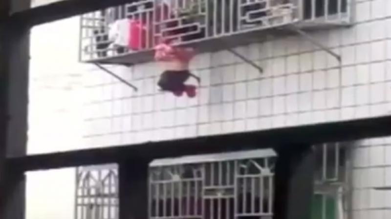 The child hanging solely by her head that was trapped in the burglar grille, while her body hung outside, crying and frantically dangling her legs in the air. (Photo: Videograb)