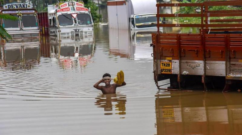 A person stands near submerged trucks on a waterlogged street at a flood-affected region following heavy monsoon rainfall, in Kochi on Thursday. (Photo: PTI)