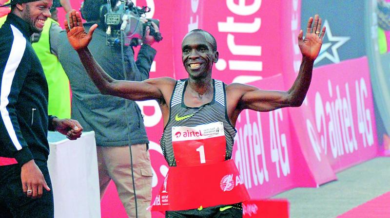 Kenyas Eliud Kipchoge crosses the finish line to win the ADHM as Jamaican sprinter Asafa Powell looks on in New Delhi on Sunday. (Photo: BIPLAB BANERJEE)