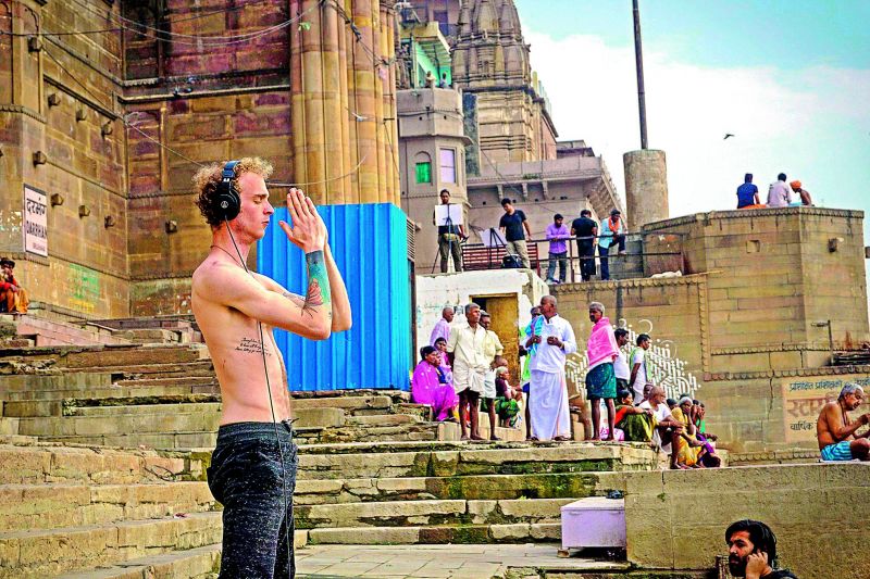 A foreign tourist listens to music while praying on the ghats of Varanasi.