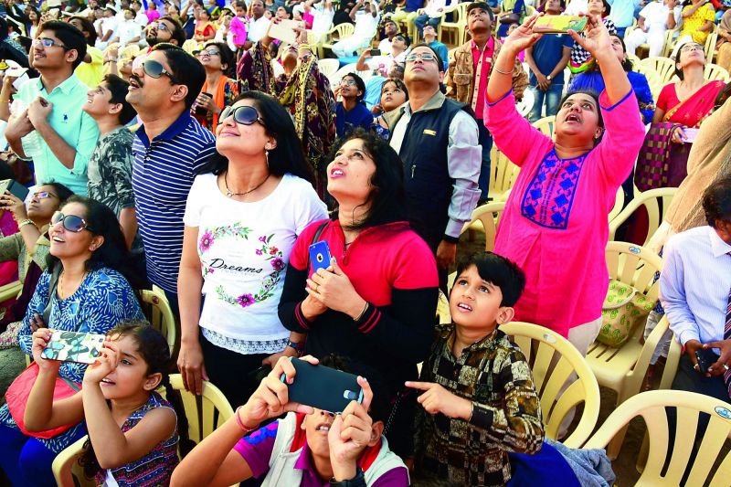 Children, along with elders, take photos of operations by the navy personnel on their mobile phones. (Photo: P. Narasimha Murthy)