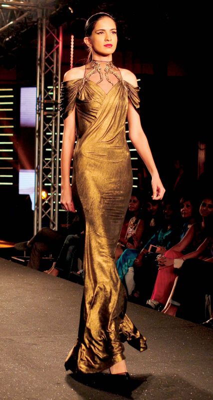 The model is seen wearing a shimmery gold cold-shoulder dress.