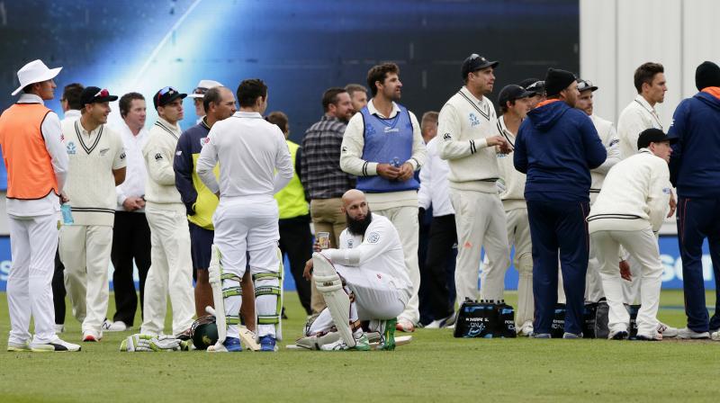 Players and officials wait on the field after the main grandstand and public viewing areas were cleared by security staff during the first Test. (Photo: AP)