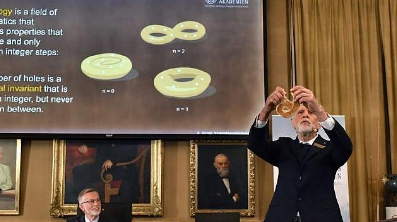 Professor Thors Hans Hansson gives a demonstration using a bagel to explain the work of the winners of the Nobel Prize in physics, at the Royal Swedish Academy of Sciences, in Stockholm, Sweden. (Photo: AP)
