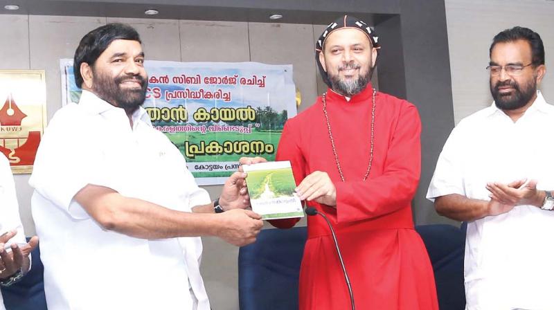 Bishop Geevarghese Mar Koorilose hands over a book  Methran Kayal- Haritha Keralathintey Veendeduppu to V. N. Vasavan, ex-MLA in Kottayam on Monday, Siby George, the writer is also seen. (Photo:  DC)