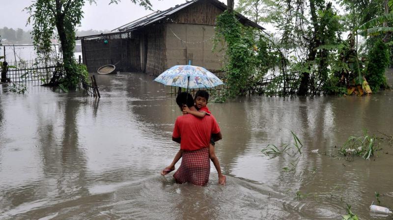 Assam Monsoon flood Lakhimpur: A father carrying his son through the flood water in Lakhimpur, Assam on Saturday. (Photo: PTI)