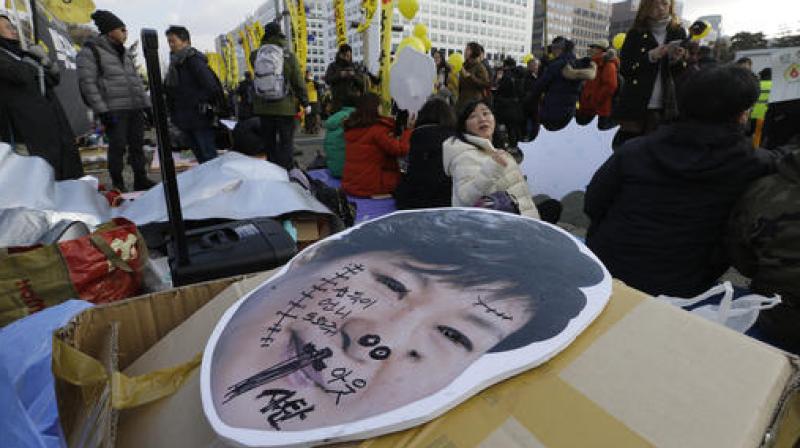 A defaced portrait of South Korean President Park Geun-hye is seen as protesters sit demanding the parliamentary impeachment of Park in front of the National Assembly in Seoul, South Korea. (Photo: AP)