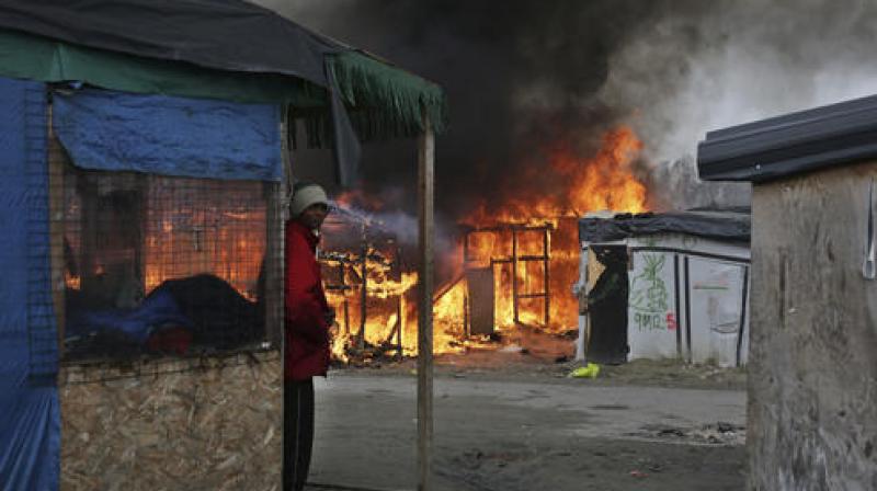A man stands next to a burning tent as fires were started in the makeshift migrant camp known as the jungle near Calais, northern France .(Photo:AP)