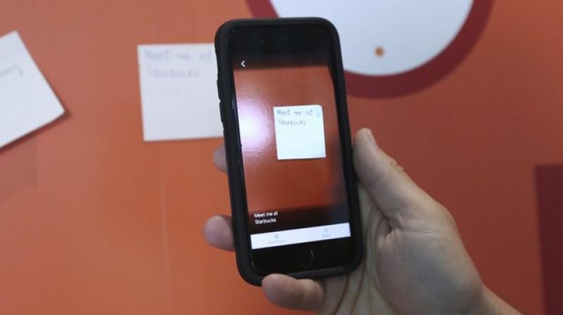 Paul Bepey uses a phone app created by Microsoft to audibly describe a drink in a can during an interview with The Associated Press at Microsoft offices in London, Friday, July 27, 2018. Improvements in artificial intelligence, combined with the decreasing cost of hardware, are making it possible for inventors to develop new products without the need for the deep pockets of governments or big corporations. With the help of 3D printers and the increased processing power of home computers, they are creating devices designed for people with motor, vision, hearing and cognitive impairments. (AP Photo/Robert Stevens)