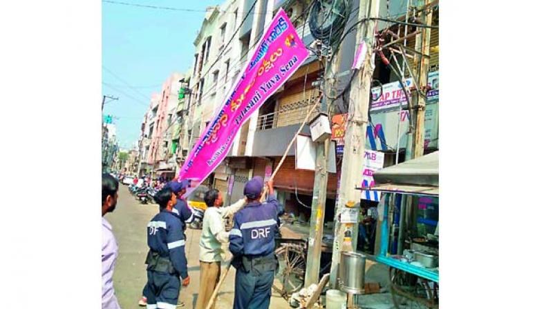 Officials remove political banners and hoardings in line with the election code, on Sunday.  (Image DC)