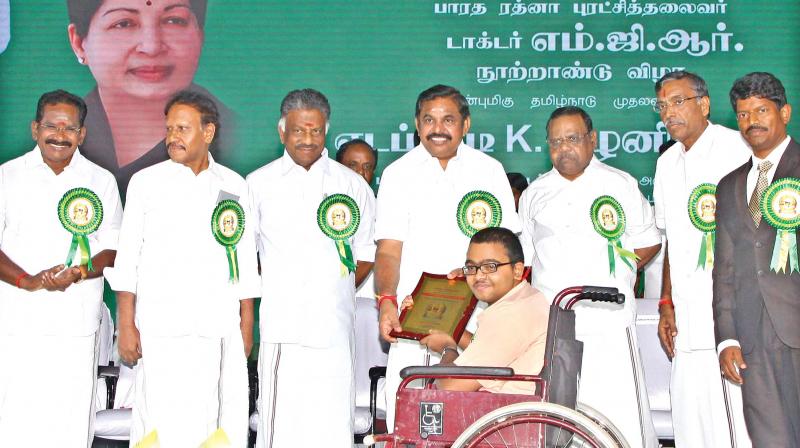 Chief Minister Edappadi K. Palaniswami presenting an award on Saturday to a physically challenged person, who was among the several winners in the various competitions held in connection with MGR centenary celebrations at Dharmapuri. Deputy CM O.Panneerselvam and Assembly Speaker P. Dhanapal were among the dignitaries present on the dais. (Photo: DC)