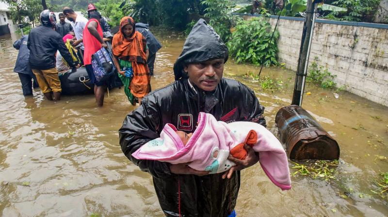 A rescuer carries an infant as people are evacuated from a flood-hit locality in Kochi on Wednesday. (Photo: PTI)