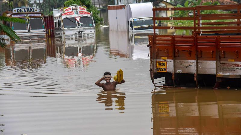A person stands near submerged trucks on a waterlogged street at a flood-affected region following heavy monsoon rainfall, in Kochi on Thursday. (Photo: PTI)