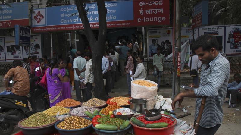 A snacks vendor check his mobile phone while anticipating customers as people stand in a queue to exchange discontinued currency notes outside a bank in Hyderabad. (Photo: AP)