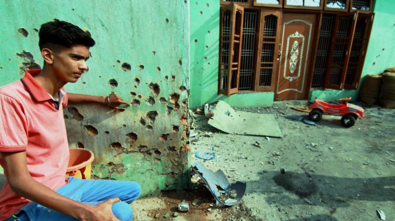 A villager showing the pockmarked wall of a building damaged by alleged shelling from the Pakistani side at Rangoor camp in Ramgarh sector, Jammu. (Photo: PTI)
