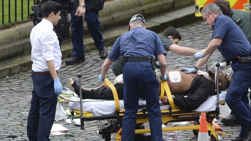 A man is treated by emergency services, as knives lie on the floor, with police looking on at the scene outside the Houses of Parliament London. (Photo: AP)