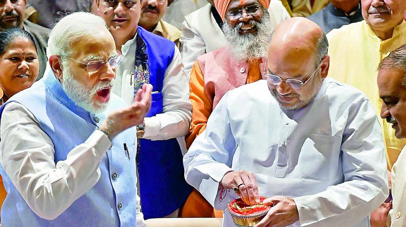 Prime Minister Narendra Modi eats Tirupati laddu prasadam offered by BJP president Amit Shah during the BJP parliamentary party meeting in New Delhi on Thursday. (Photo: PTI)