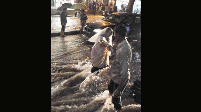 A yougester helps a woman cross the water-logged road at Shivananda Circle in Bengaluru on Friday 	(Photo: KPN)