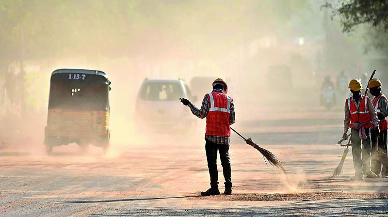 Sweepers on the road opposite Uppal stadium on Saturday rake up a thick blanket of dust, causing inconvenience to motorists and pedestrians along the way. (Photo: Chand Ahmed)