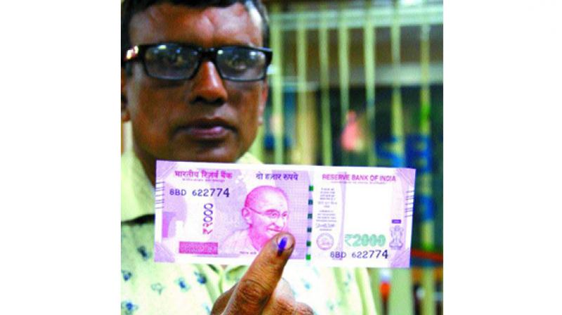 A customer shows a new 2,000 note he exchanged at the SBT bank at Paramekkavu after ink was applied on his finger at Thrissur on Thursday. (Photo: DC)