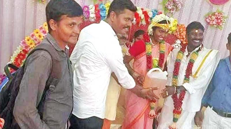 Prabhu(left), gives Elanchezhian and his astonished  just-wedded wife Kanimozhi 5 litres of pertrol, in a can, as a gift on their wedding day. (Photo:DC)