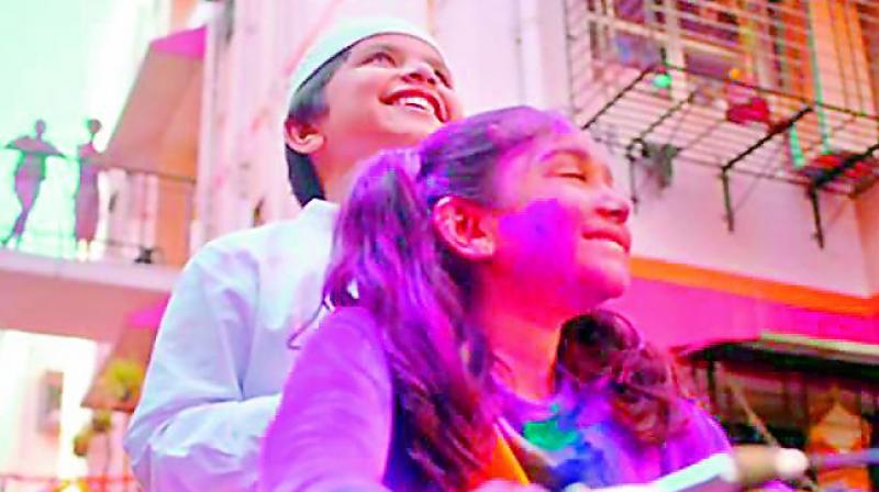 A screenshot of the Surf Excels one minute-long commercial, which features a young Hindu girl, dressed in a white t-shirt, choosing to get stained in Holi colours in order to protect her young Muslim friend who has to go to the nearby mosque to pray.