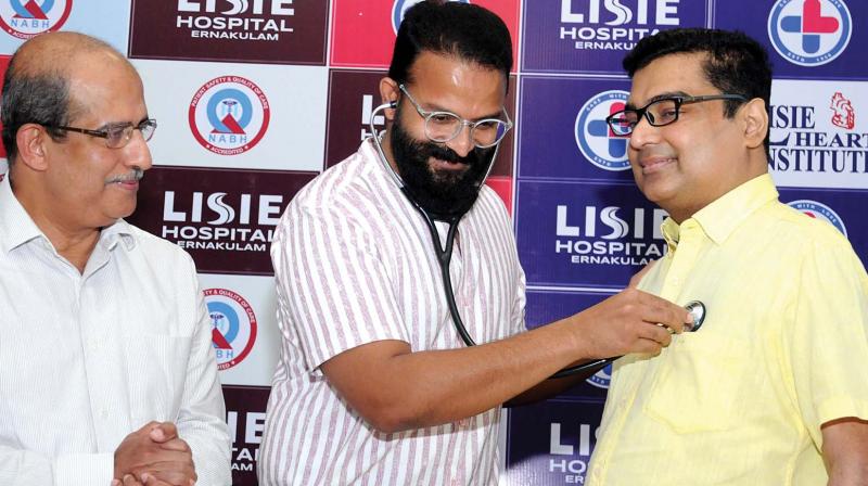 Actor Jayasurya tries a steth he borrowed from Dr Jose Chacko Periyapuram to check on heartbeats of Girish Kumar, who had undergone two heart transplants, at the event marking his fifth year after surgeries at Lisie Hospital, in Kochi on Wednesday.    (ARUN CHANDRABOSE)