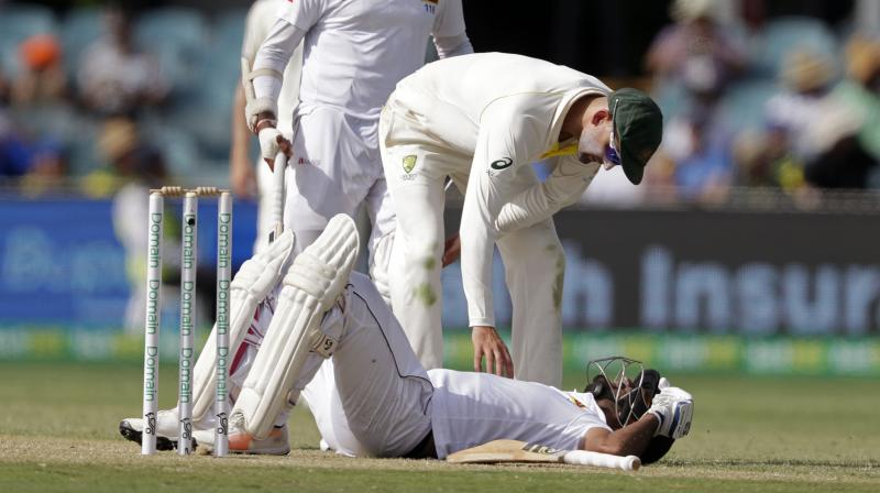 Australias Nathan Lyon bends over to check on Sri Lankas Dimuth Karunaratne after he was struck in the head by a delivery from Pat Cummins on day 2 of their cricket test match. (Photo: AP)
