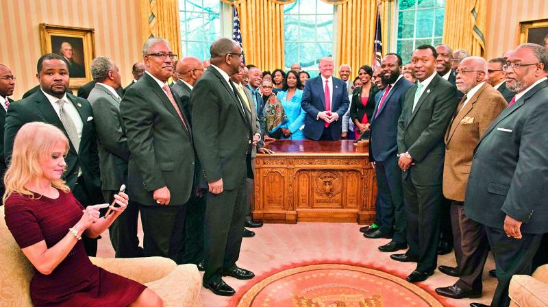 President Donald Trumps top aide Kellyanne Conway checks her phone after taking a photo of US President Donald Trump and leaders of historically black universities and colleges in the Oval Office. Ms Conway came under fire for casually kneeling on a couch in the Oval Office with Twitteratis berating her for lack of respect. (Photo: AFP)