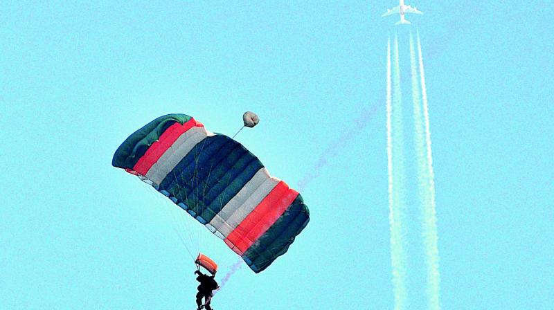 Sky divers of Indian Navy display safe landing as a domestic airplane flies above them during the operations display as part of Navy Day at Ramakrishna Beach in Visakhapatnam on Monday.